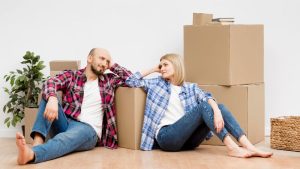 Sala de estar moderna e compacta com sofá claro, mesa de centro de madeira, estante embutida cheia de livros e plantas, iluminação natural à direita.
